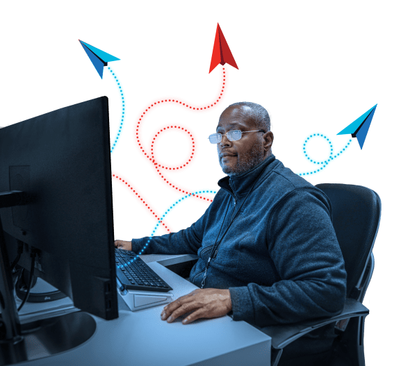 Man sitting in front of his computer at his desk with airplane icons representing the Software Factory floating above him