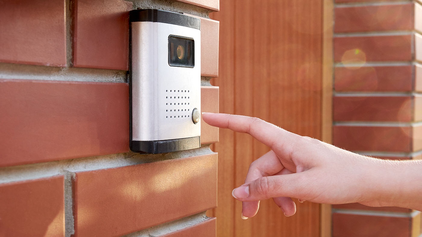 A hand pressing the button on an exterior digital doorbell
